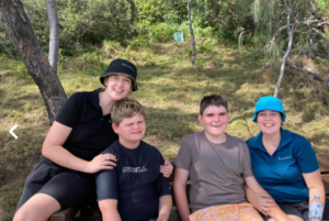 four people sitting on a bench in the bush, two ladies caring for two teenage boys with Angelman syndrome, everyone is smiling